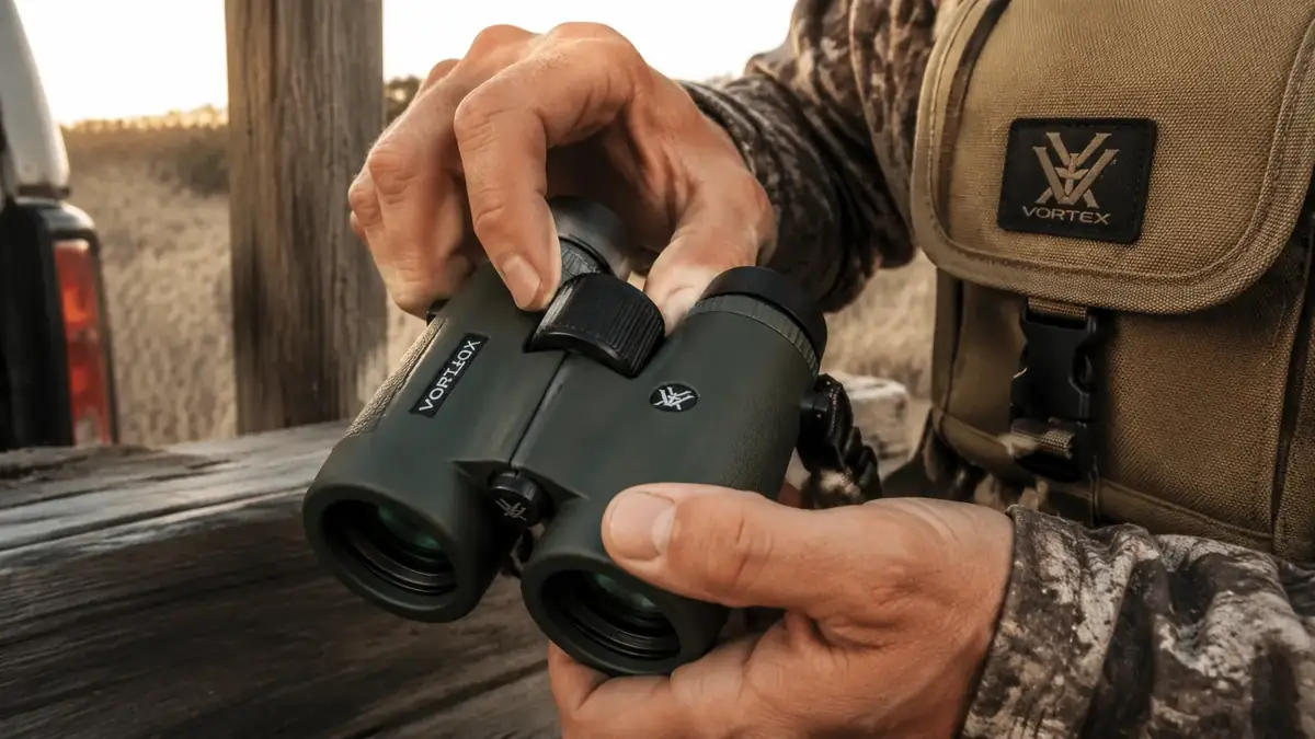 Hands adjusting the diopter and focus wheel on a pair of 10x42 binoculars in dim light