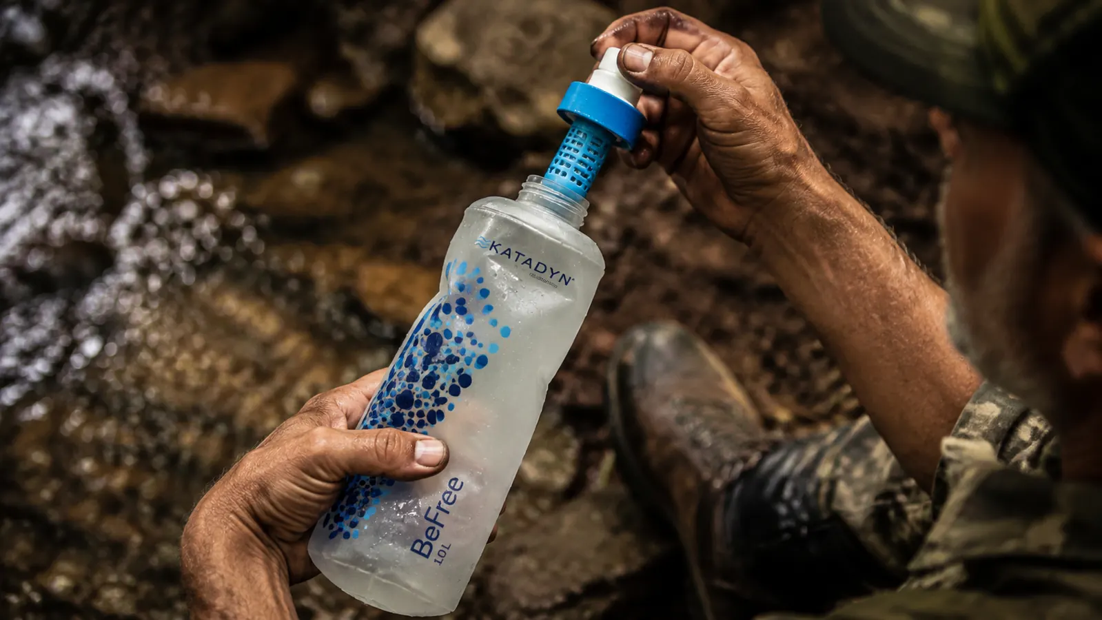 Hand screwing a squeeze filter cap onto a soft water flask beside a trail pack